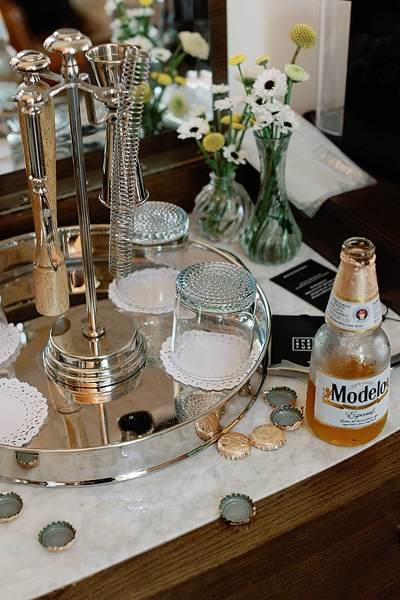 Wedding bar cart styling with a silver tray, cocktail shaker, jars, and daisy bud vases on a marble countertop by a mirror