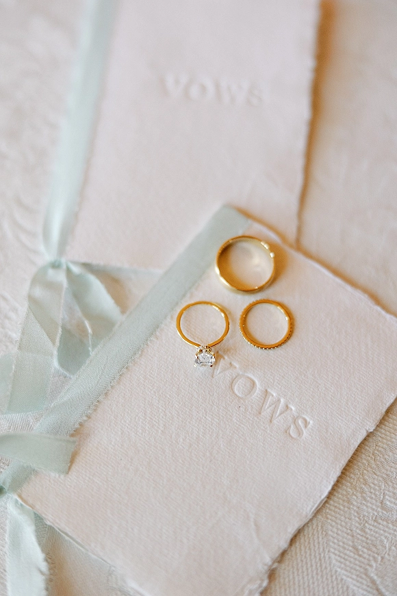 Wedding rings and gold wedding band set with a diamond engagement ring on vow books, tied with a light blue silk ribbon on fabric surface