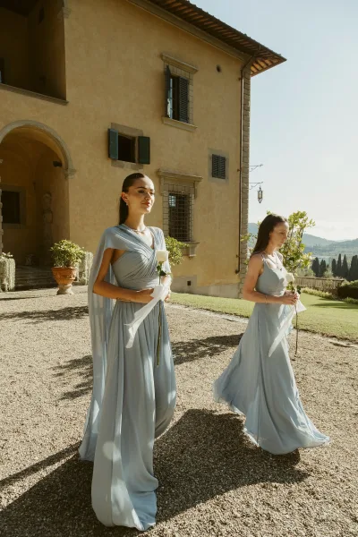 Bridesmaid portrait in dusty blue bridesmaid dresses holding white roses with ribbon streamers, posed by a stucco villa courtyard entryway