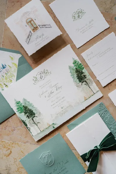 Wedding invitation suite featuring watercolor wedding invitations with a monogram crest, arranged on a stone tile surface.