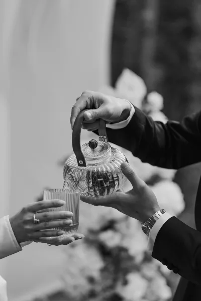 Wedding tea ceremony pouring tea ritual as the groom gently pours from a glass teapot for the bride in a close-up, intimate moment