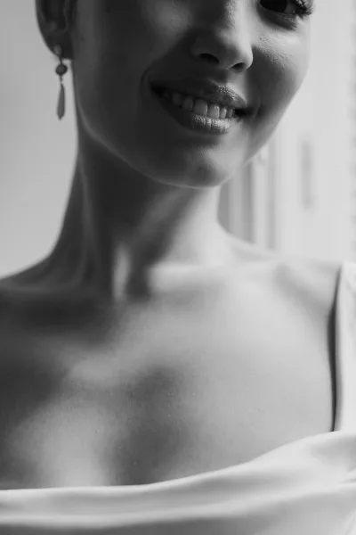 Bridal portrait capturing a bride's smile in close-up, her delicate dangle earrings glinting in soft window light.