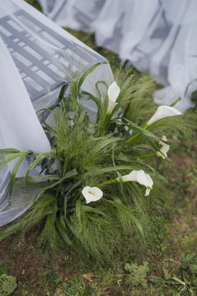 Ceremony aisle flowers with a calla lily aisle arrangement lining the grass lawn, formed into low, grounded clusters.