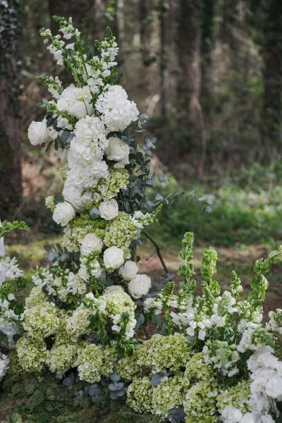Ceremony floral installation of outdoor ceremony florals with white roses, set against forest trees and the woodland floor.