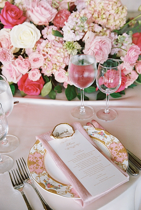 Reception tablescape with pink wedding tablescape details, gold-rim floral china, blush menu and place card, and pink centerpiece on white linens