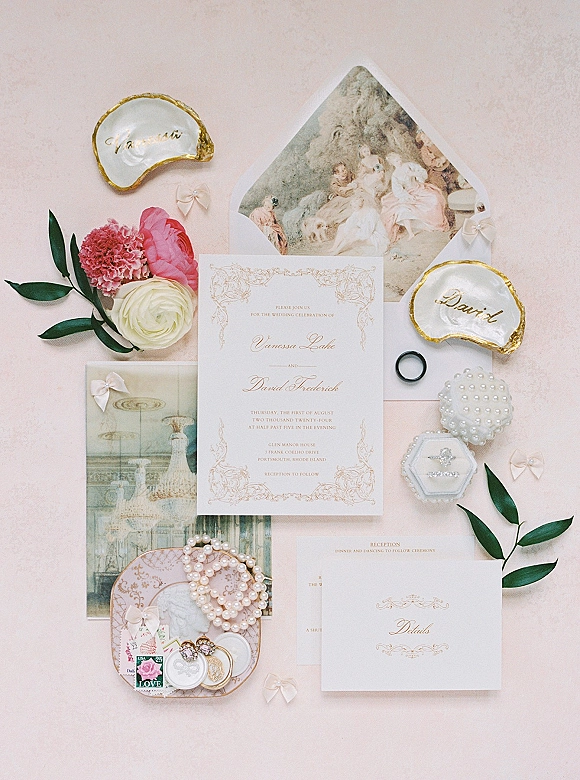 Invitation suite wedding invitation flat lay with wax seal, vintage stamps, pearls, rings, ribbon bows and florals on a pink fabric backdrop