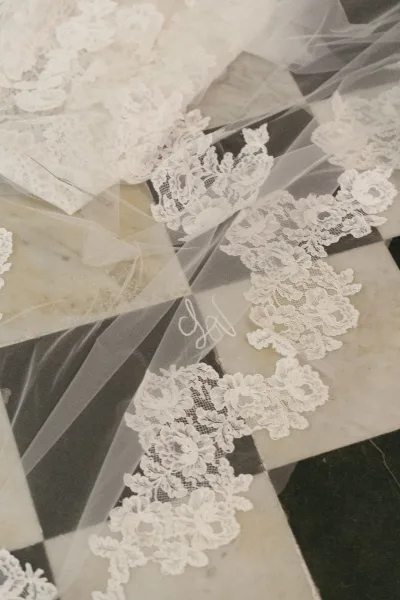 Lace wedding veil with cathedral lace veil edge, monogram embroidery on soft tulle laid out on a black-and-white checkered tile floor