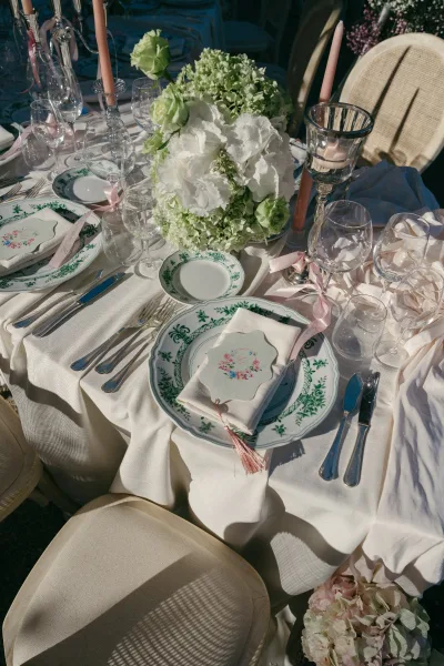 Reception tablescape with a wedding table setting, hydrangea centerpiece and pink taper candles on white linen in sunlit garden seating area