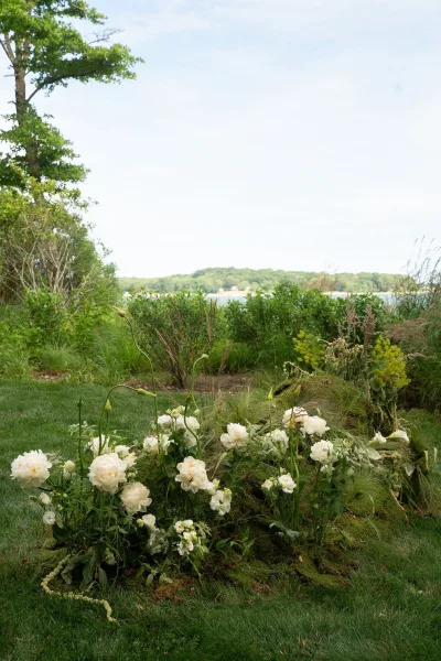 Wedding ceremony flowers in a ground floral arrangement of white blooms and greenery with moss accent on a lakeside lawn under open sky