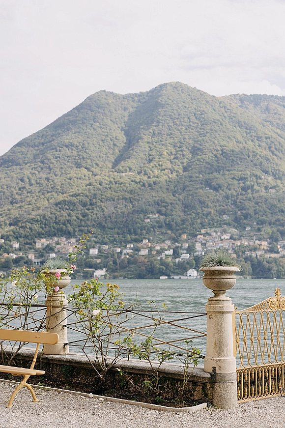 Wedding venue view of a lake wedding venue from a stone balustrade terrace with urn planters and rose bushes, mountains beyond