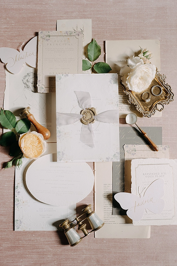 Wedding invitation suite with wax seal wedding invitations, chiffon ribbon and rose accents arranged on a linen fabric backdrop flat lay