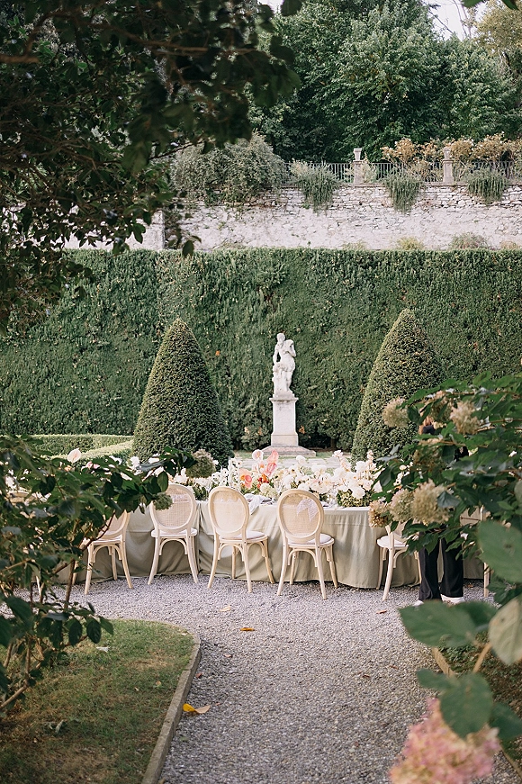 Reception tablescape with an outdoor wedding reception table on a long banquet setup, sage green tablecloth, florals and candles in a formal garden
