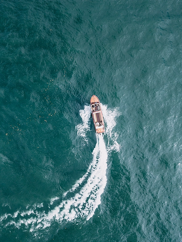 Wedding getaway boat speeding across open ocean, wooden speedboat cutting a bright white wake during a wedding boat exit