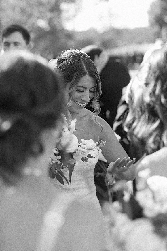 Bride portrait in a black and white wedding portrait, smiling while holding a bouquet in a strapless lace dress among guests outdoors
