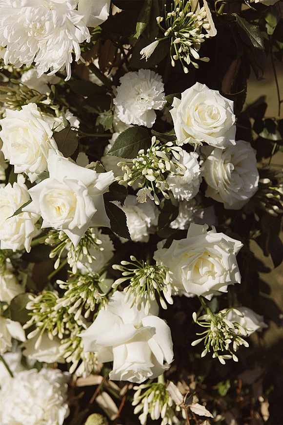 Wedding flowers with a white rose bouquet of roses, carnations, and greenery foliage resting on sunlit ground with soft shadows