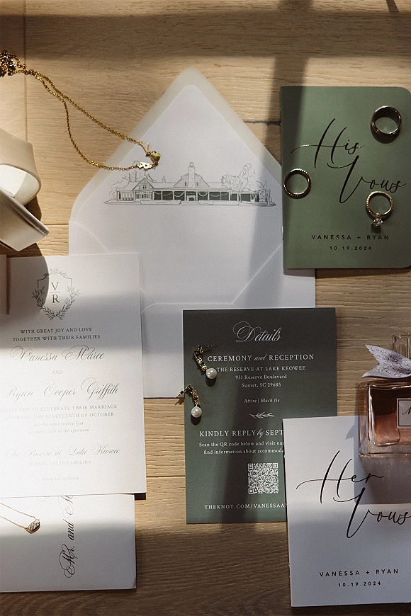 Invitation suite wedding invitation flat lay arranged with envelopes, vow booklets, rings and jewelry on a wood tabletop in sunlight shadows