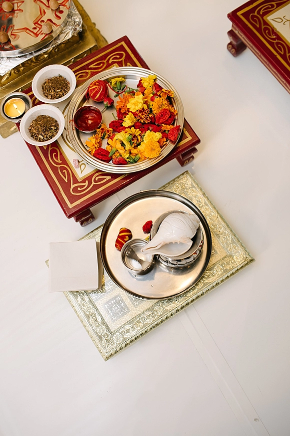 Wedding ritual tray arranged on a white tabletop with marigold flowers, petals, small bowls of kumkum, and a tea light candle accent