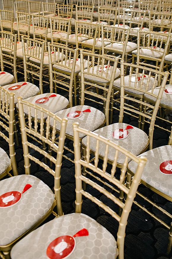 Ceremony seating with wedding chair decor on gold Chiavari chairs, patterned cushions, and round fan programs with red tassels indoors