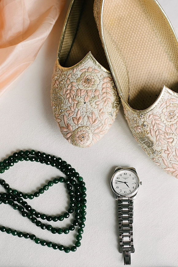 Wedding shoes and bridal flats in a flat lay with embroidered details, a green beaded necklace and silver wristwatch on a light surface