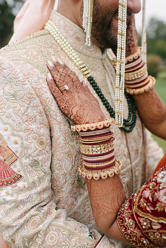 Wedding couple portrait of an indian wedding couple as the bride’s mehndi hands with red bangles and ring rest on the groom’s embroidered sherwani outdoors