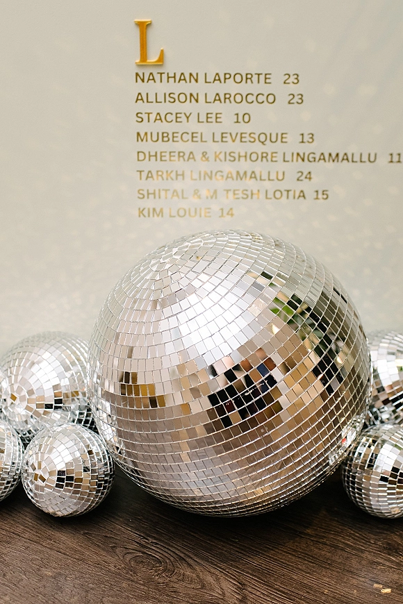 Wedding seating chart acrylic seating chart sign with gold vinyl monogram lettering, set on a wood floor beside mirrored disco balls