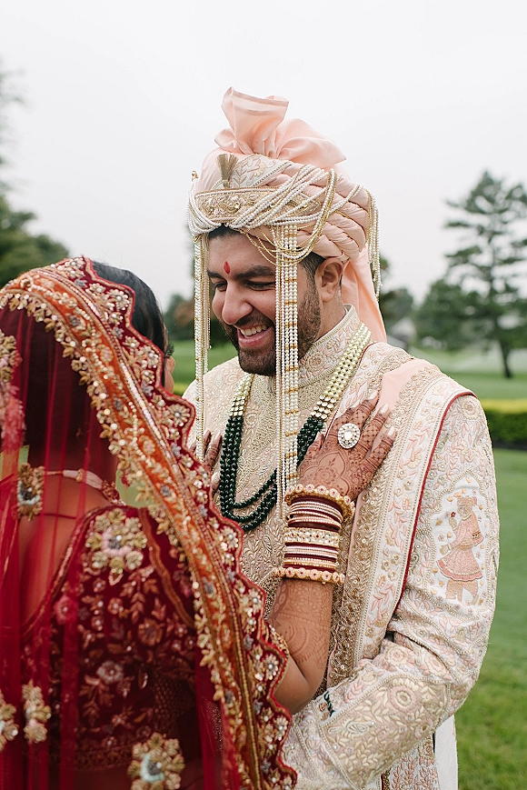 Wedding couple portrait of a south asian wedding couple embracing as the bride holds the groom’s face on an outdoor lawn with trees and sky