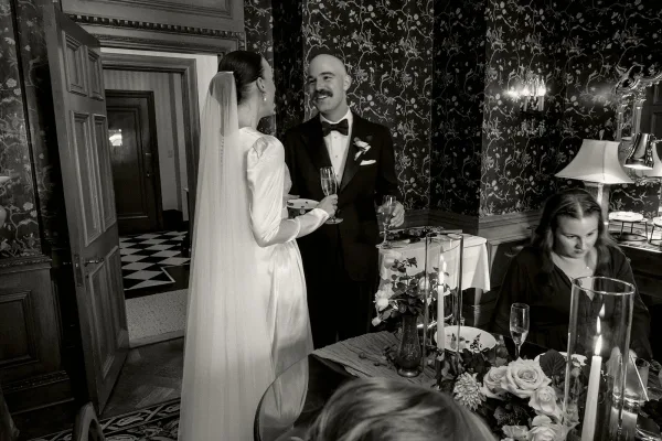 Reception moment in a black and white wedding photo as the bride and groom share a toast, champagne flutes raised as the bride faces the groom.