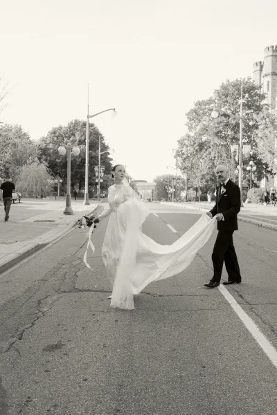 Couple portrait on a city street, an urban wedding portrait with the bride holding a bouquet as the groom walks beside her.