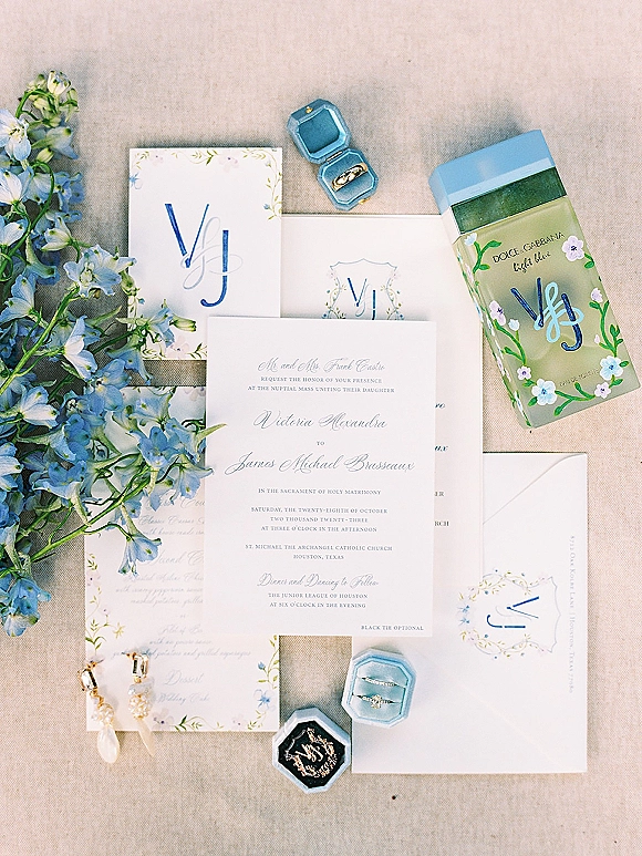 Wedding invitation suite with blue floral invitations, monogram cards, envelopes, gold wedding bands and pearl earrings on linen backdrop