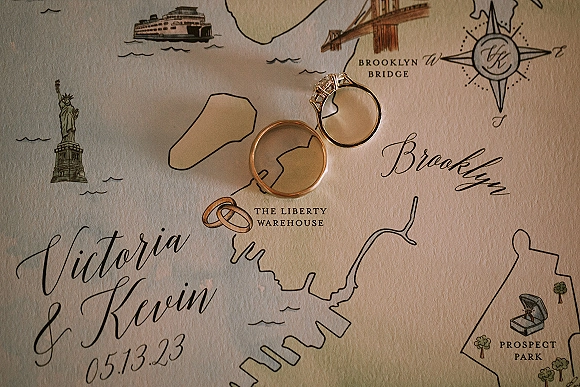 Wedding rings and engagement ring on invitation, gold wedding bands resting on calligraphy text over an illustrated map background