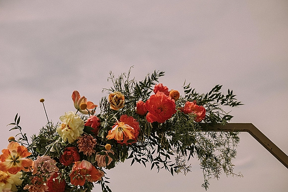 Wedding arch flowers cascade on an asymmetrical wedding arch with lush greenery on a metal frame against the open sky backdrop