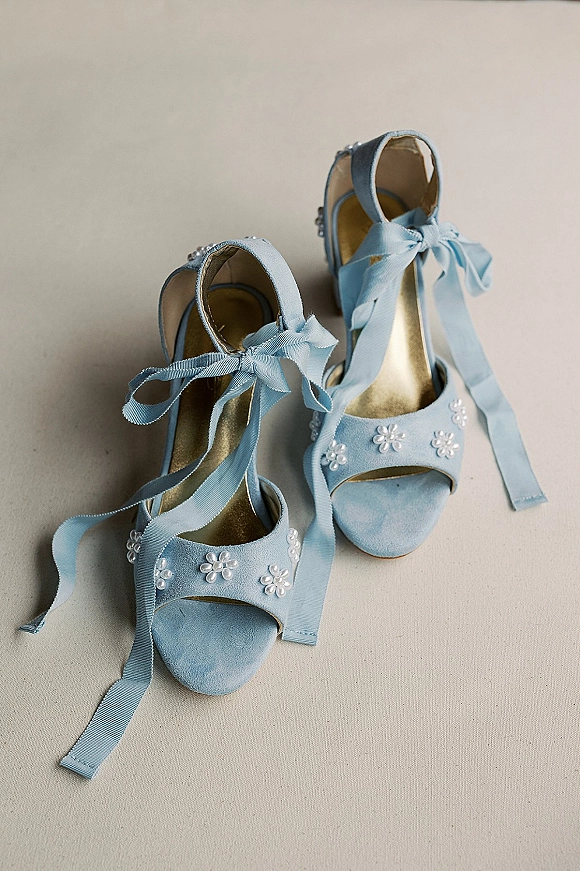 Bridal shoes with something blue satin ribbon ties and pearl flower embellishments, open-toe heels styled on a neutral fabric backdrop