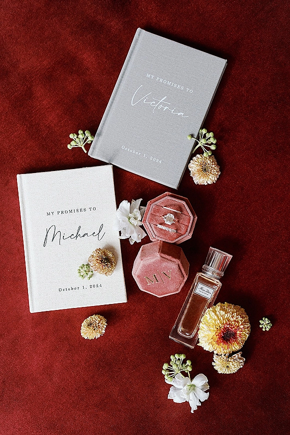Wedding vow books with personalized vow book covers styled beside a velvet ring box and rings on a red velvet fabric backdrop