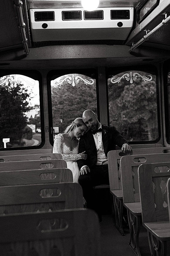 Couple portrait of bride and groom on trolley, her lace sleeves and ring visible as she rests on him by tram windows and wooden seats