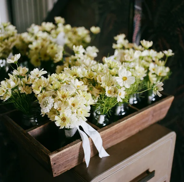 Wedding bouquets of white wildflowers tied with white ribbon, arranged in glass jars on a wooden drawer against a dark wall
