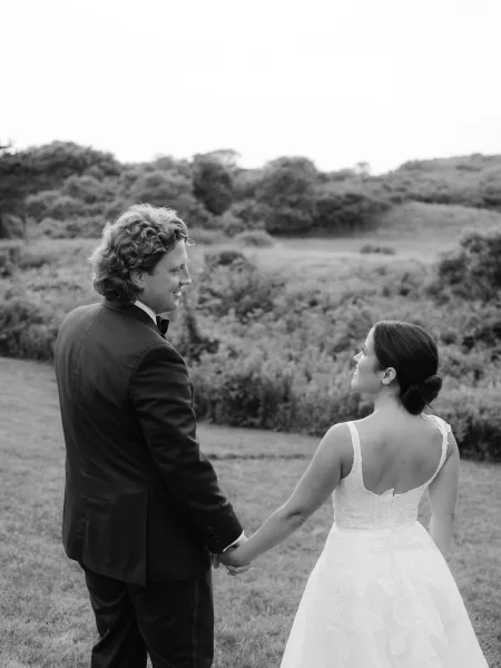 Couple portrait in a black and white wedding portrait, bride and groom holding hands in a grassy field with rolling hills and sky behind
