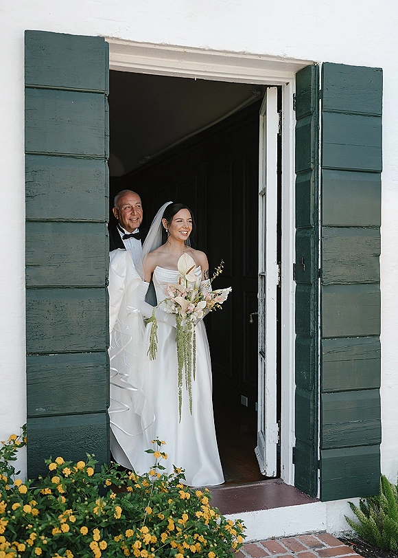 Bridal portrait of a bride holding bouquet with a long veil and calla lily greenery arrangement in a doorway with green shutters