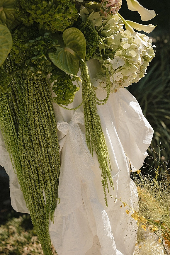 Bridal bouquet with a cascading bridal bouquet of white hydrangea and trailing green amaranthus, tied with ribbon, in sunlit garden foliage