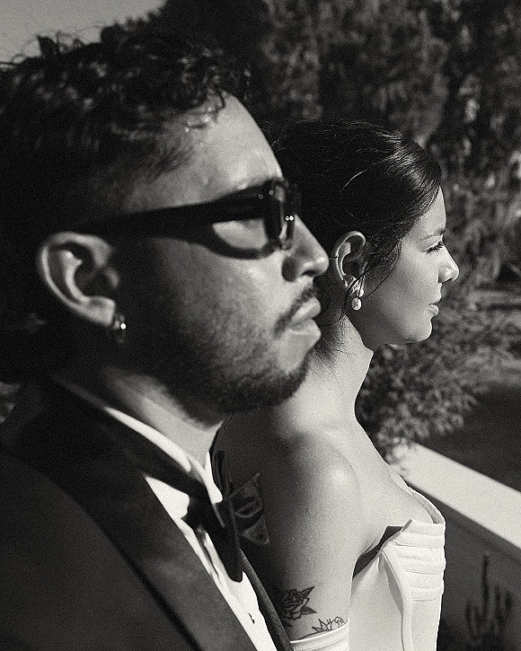 Couple portrait in a black and white wedding portrait style, bride in strapless dress and groom in sunglasses on a sunlit hillside