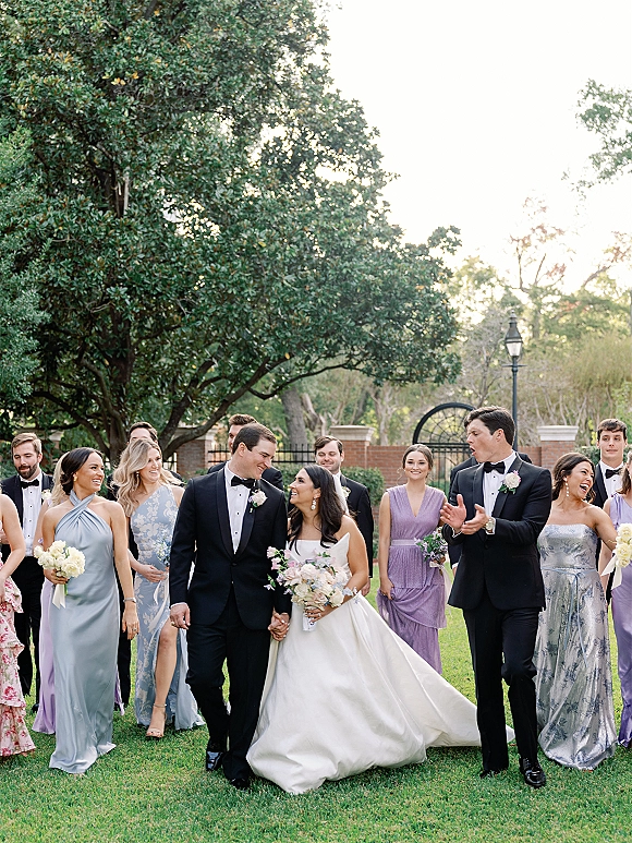 Wedding party portrait of bride and groom with wedding party walking on a garden lawn, bride holding bouquet, tuxedos and dresses behind