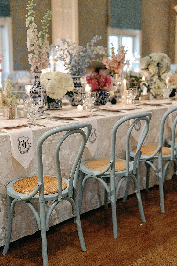 Reception tablescape with blue and white wedding table vases, hydrangea florals, taper candles, and place settings in a bright indoor room with windows
