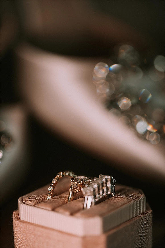 Wedding rings and engagement ring close up in an open ring box, showing gold bands and a diamond ring against dark bokeh lights