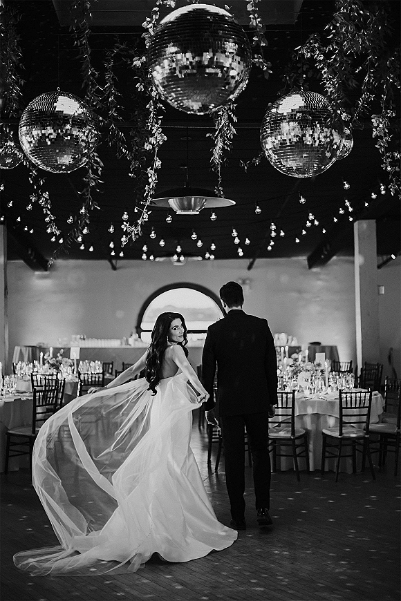 Couple portrait of bride in a strapless wedding dress and long veil with groom in black suit on a reception dance floor under disco balls