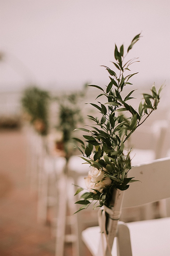 Ceremony aisle decor with greenery chair garlands and aisle chair florals, white roses in glass vases tied with ribbon on folding chairs