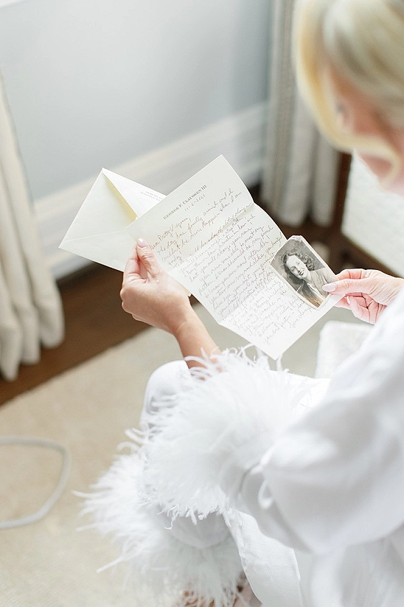 Wedding letter with a handwritten note and envelope, vintage photo tucked inside, resting on a feather-trim robe in soft window light
