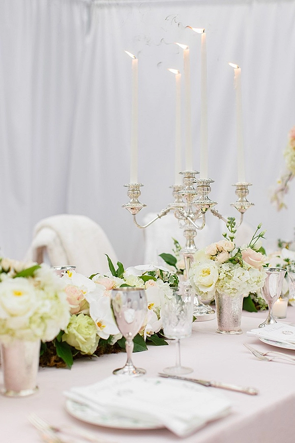 Reception tablescape with wedding table centerpiece of silver candelabra, taper candles, hydrangeas, roses and orchids on white linens with draping