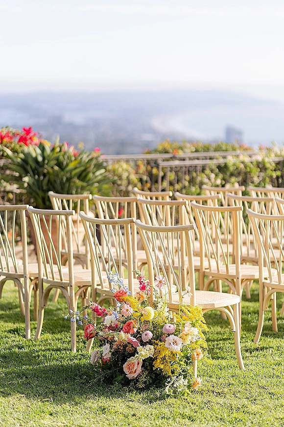 Ceremony seating with outdoor ceremony chairs in neat rows, lined with colorful aisle flowers on a lawn terrace overlooking the ocean