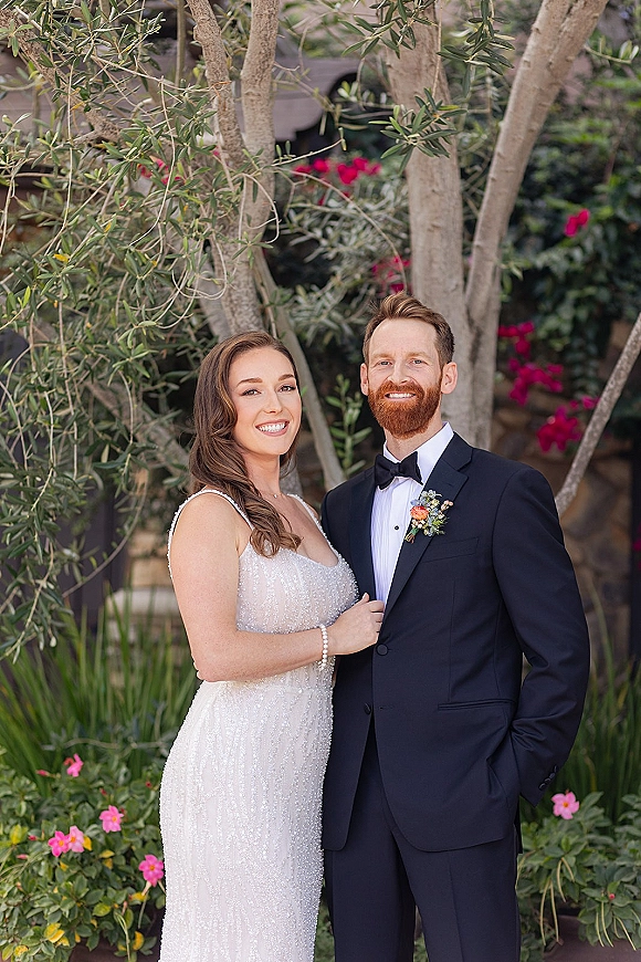 Couple portrait of bride and groom portrait smiling in a garden, bride holding his lapel, her beaded wedding dress sparkling in natural light