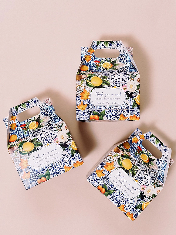 Wedding favor boxes with personalized wedding favor packaging labels featuring citrus and floral illustrations on a blue tile pattern against a blush backdrop