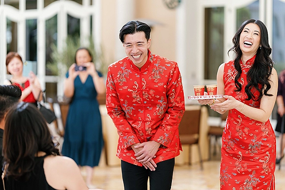 Tea ceremony moment in a Chinese wedding tea ceremony as couple serves tea with double happiness cups on a tray before guests indoors